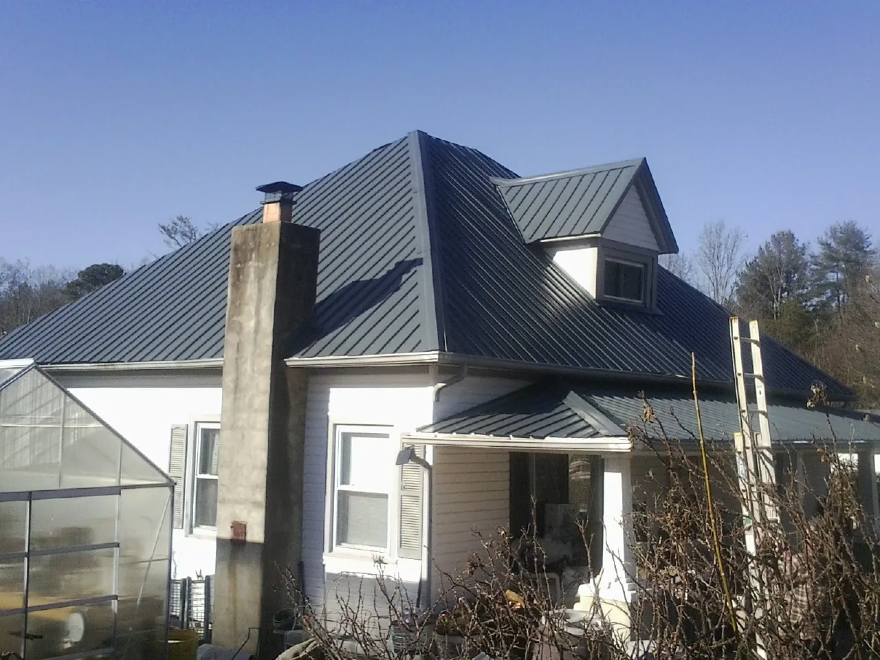 Dark blue standing seam metal roof on a white farmhouse with dormer — Slate & Tile Roof Repair by Roofing Brothers in Forestville