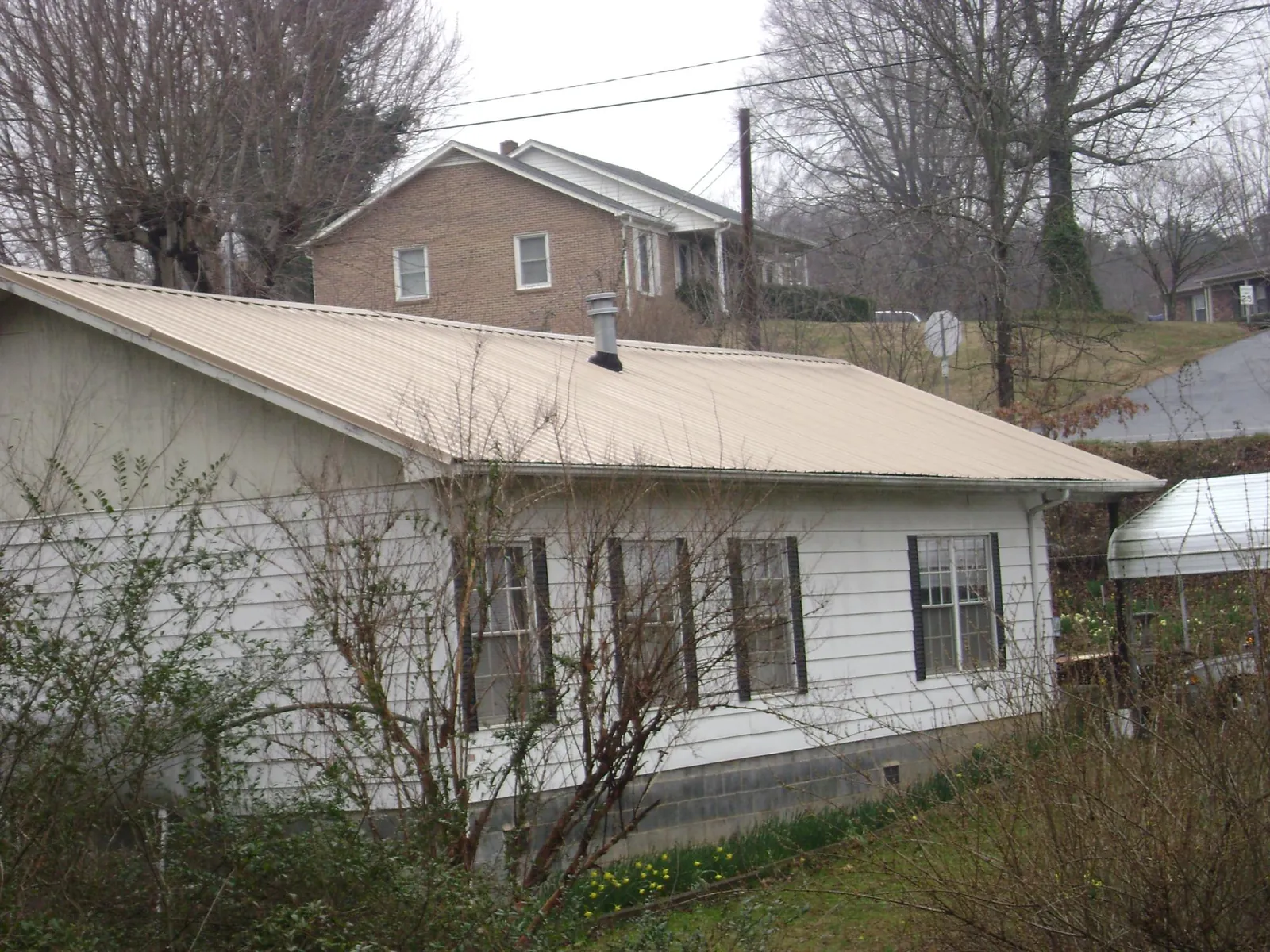 Tan metal roof on a white sided house set into a hillside — Commercial Roofing by Roofing Brothers in Forestville